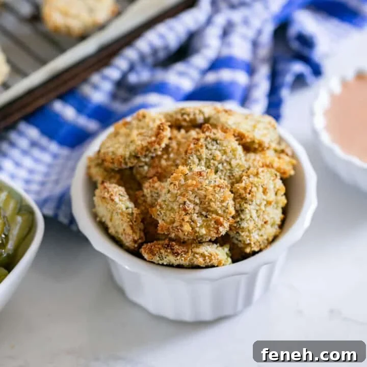 A white bowl of fried pickles with the pan behind it and a blue and white towel in the background.