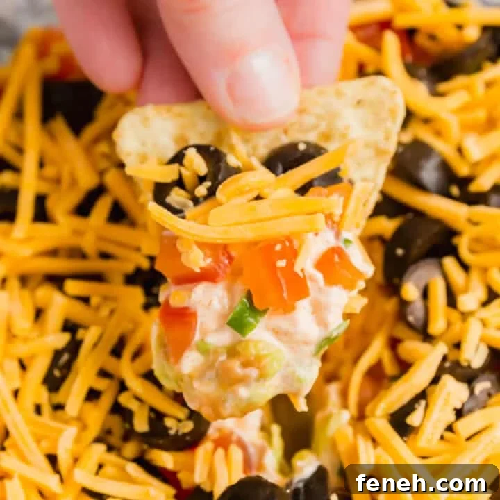A hand putting a tortilla chip up with taco dip on it.