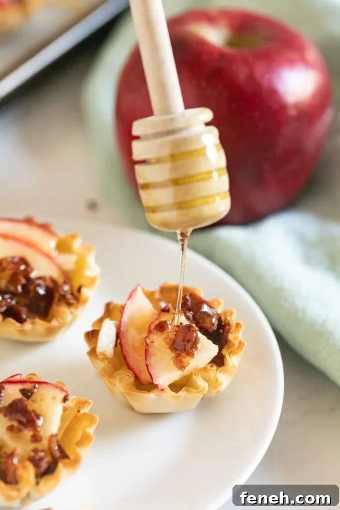 A close up image of a honey dipper drizzling honey over a brie phyllo cup.