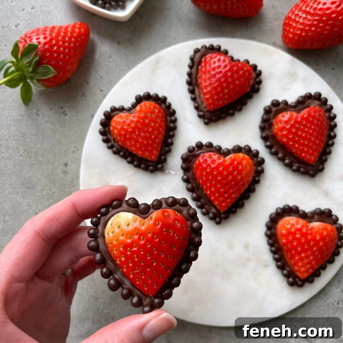 A hand holds a Strawberry Chocolate Heart with a chocolate dot border.