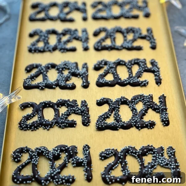 A gold tray displays several chocolate decorations shaped as “2024,” each topped with small silver sprinkles, perfect for adding a festive touch to your party bites or inspiring creative dessert recipes.