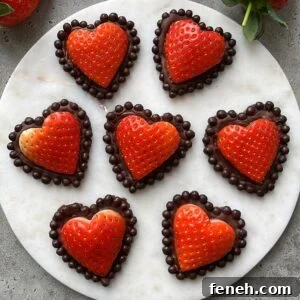 Seven heart-shaped strawberries dipped in chocolate and bordered with chocolate balls are arranged on a round white marble surface.