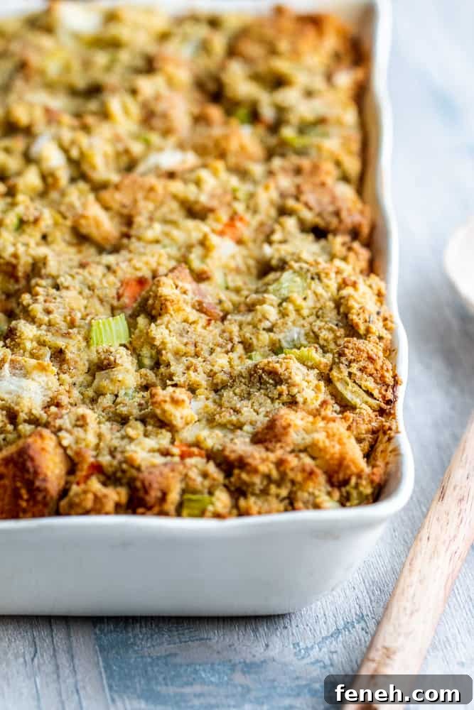 Cornbread dressing in a white baking dish with wooden spoon on the side.