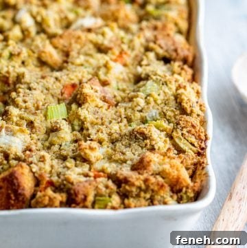 Cornbread dressing in a white baking dish with wooden spoon on the side.