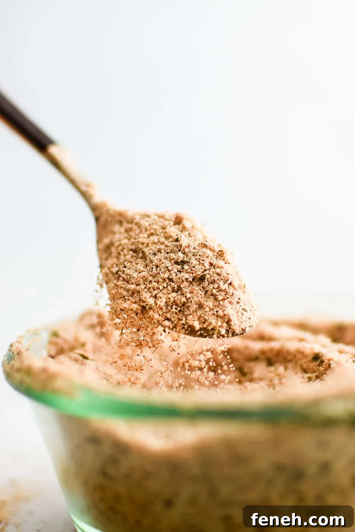 Spoon filled with homemade Shake and Bake seasoning spilling from the edges into a glass jar filled with the rest of the seasoning.