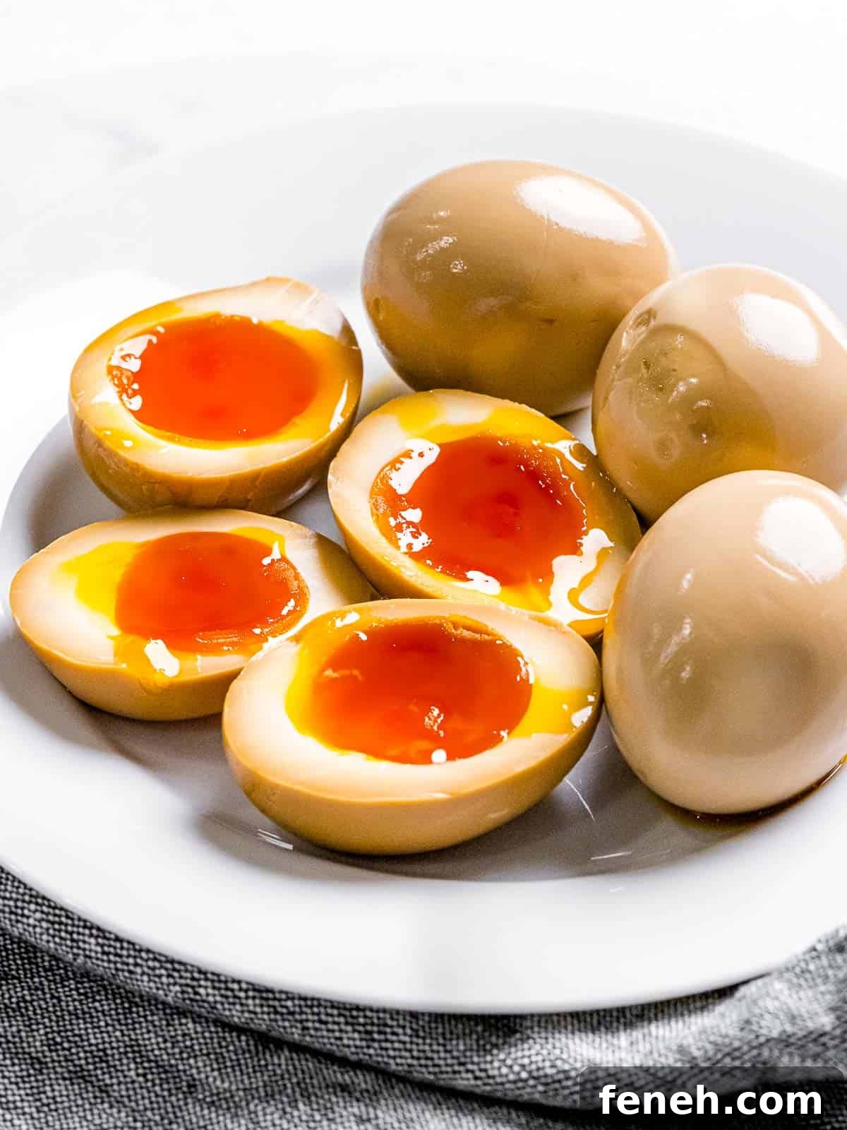 Ramen eggs marinated in soy sauce with soft boiled yolk cut in half to show orange, runny yolk on a plate.