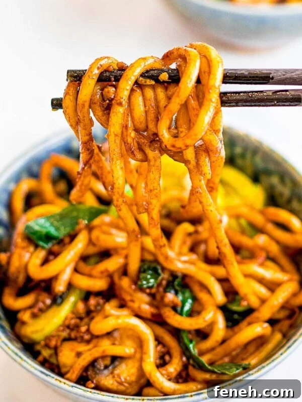 a bowl of yaki udon, stir fried udon noodles held by chopsticks