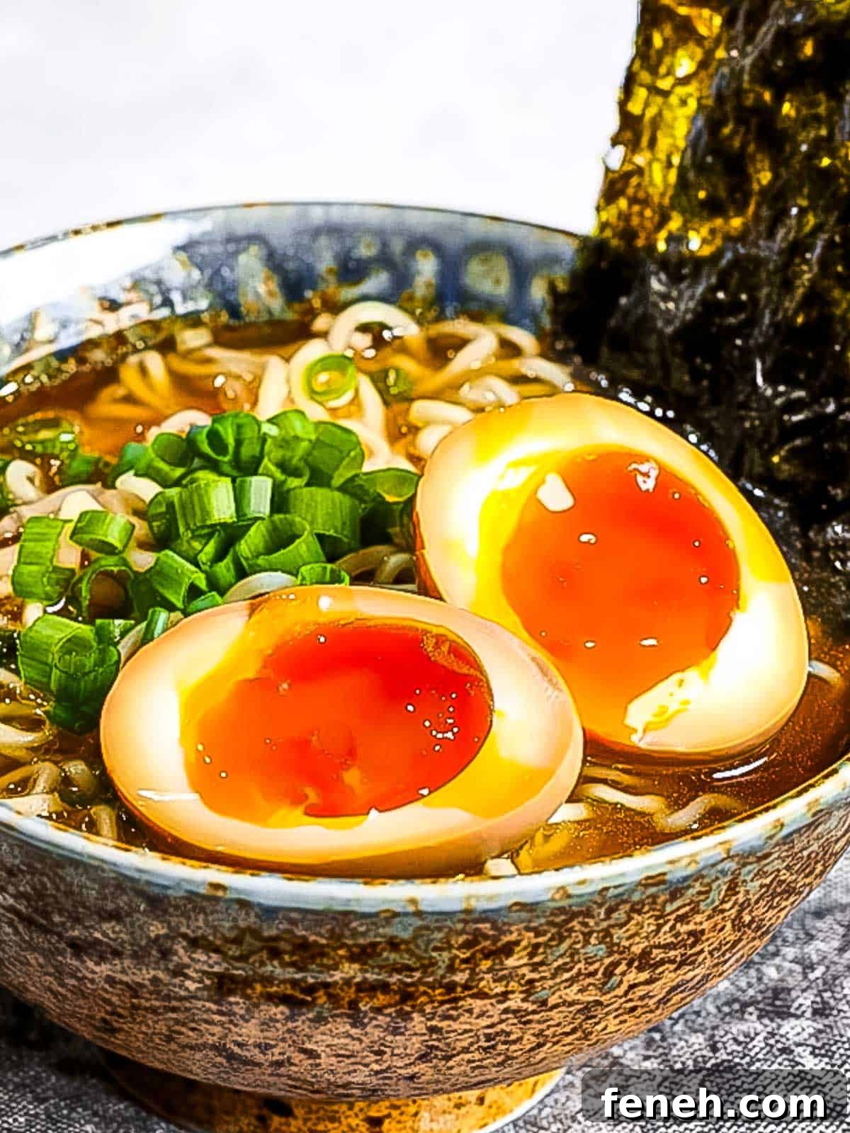 Ramen eggs (ajitama) marinated in soy sauce cut in half and placed on top of a bowl of ramen noodles garnished with green onions and nori.
