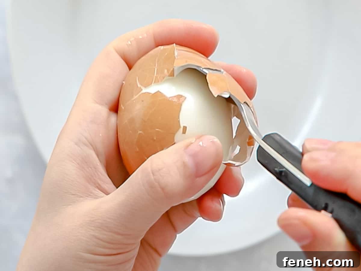 Spoon being inserted between a soft boiled egg and the shell for easy peeling.