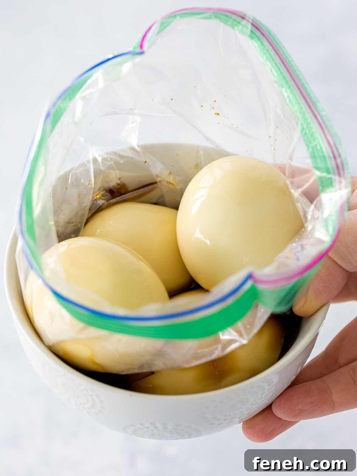 Soft boiled eggs in a soy sauce and mirin marinade inside a plastic bag set in a small bowl.