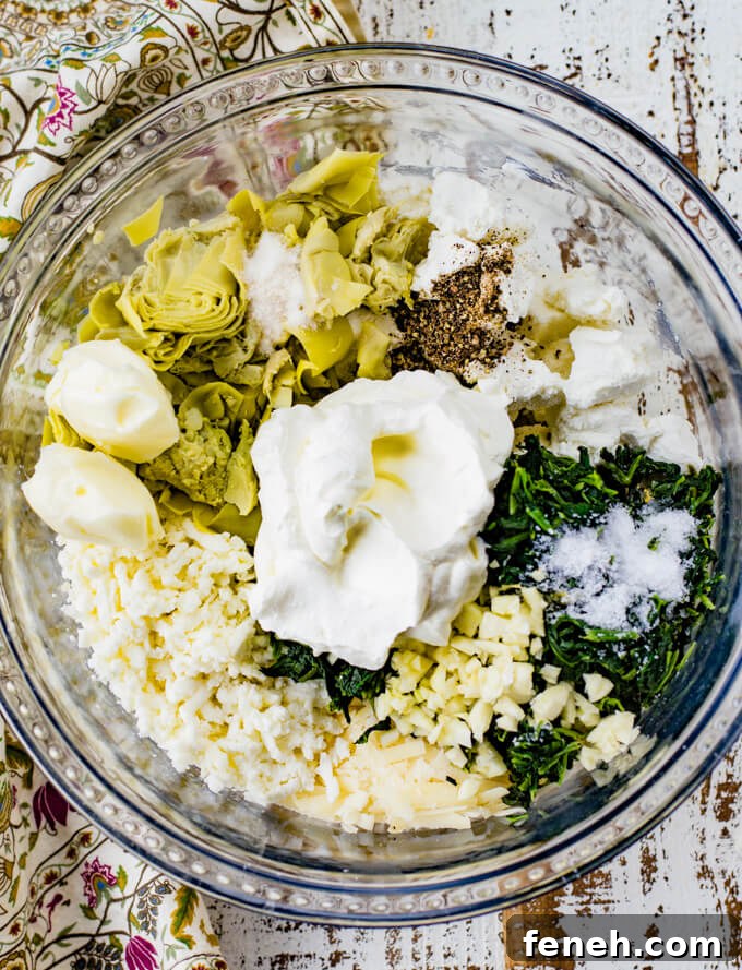 A clear mixing bowl of spinach, artichokes, cheese, sour cream, garlic salt, salt and pepper. A tan, green and purple napkin sits next to the bowl.