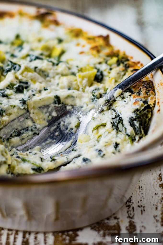 Baked Spinach Artichoke Dip in a casserole dish. A serving spoon sits in the dish.