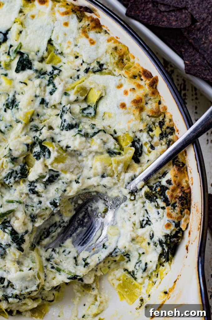 Baked Spinach Artichoke Dip in a casserole dish. A serving spoon sits in the dish.