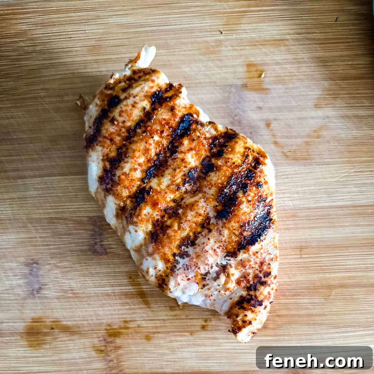 A Tajín Grilled Chicken breast sits on a wooden cutting board.