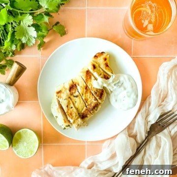 Grilled chicken with cilantro crema on a white plate surrounded by limes, cilantro, and a glass of beer.