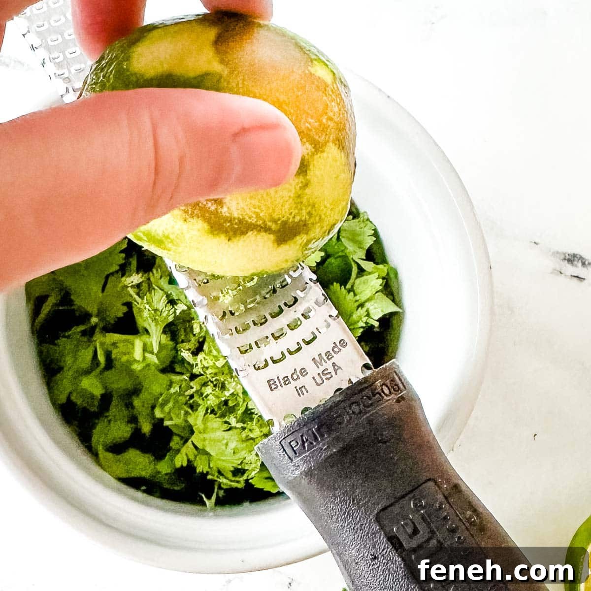 A lime is zested into a white bowl with a microplane grater.