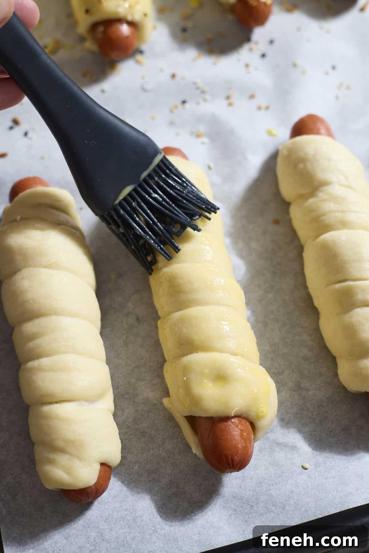 Egg wash being brushed onto a pretzel-wrapped hot dog.