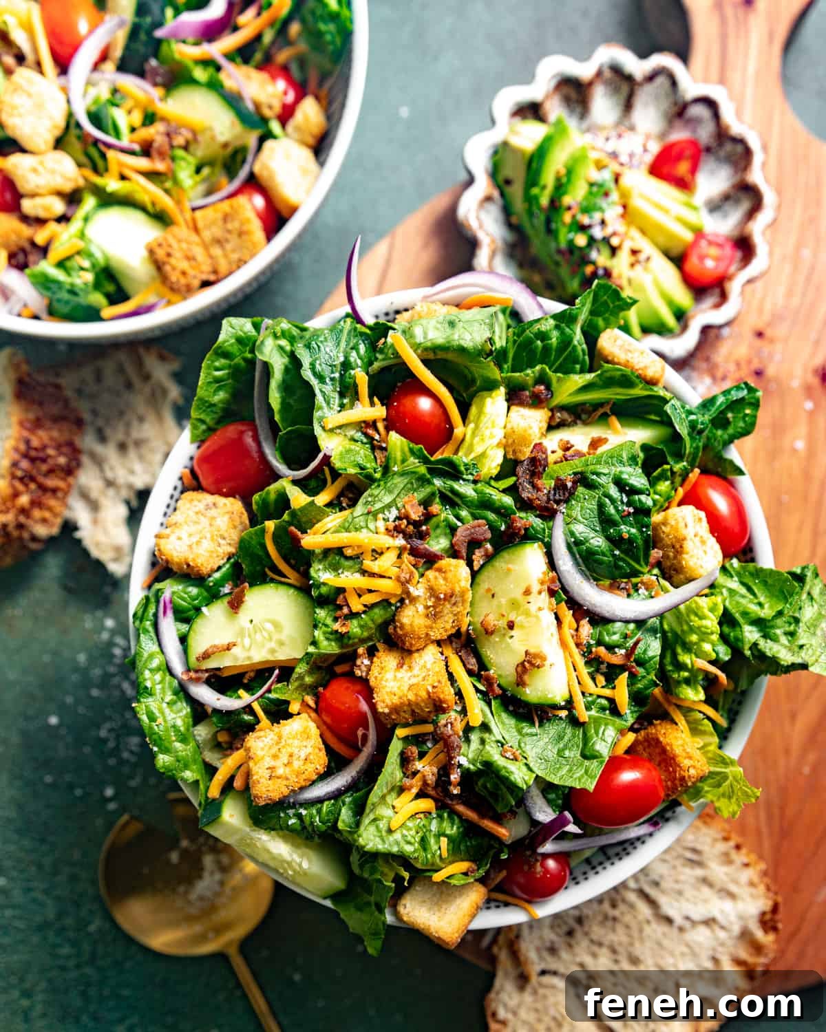 a big bowl of salad on a cutting board with a small bowl of avocado and bread.