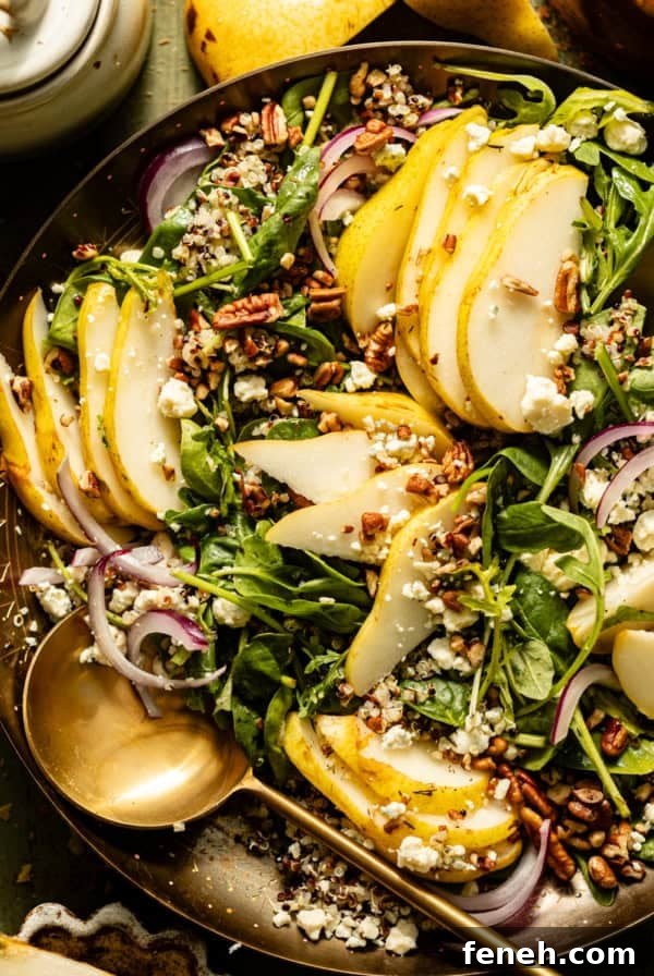 arugula pear salad in a gold dish with spoons and sliced pears next to the dish.