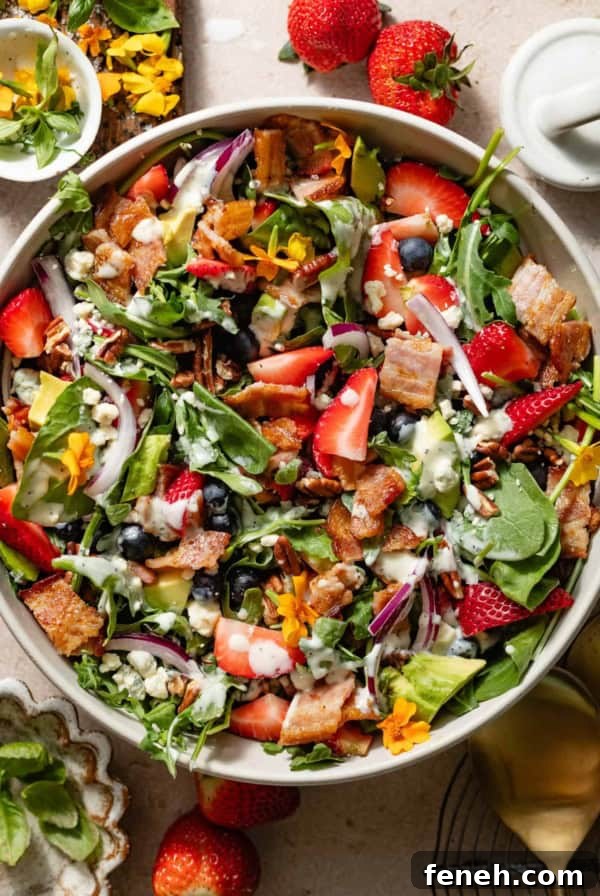strawberry pecan salad in a serving bowl topped with poppyseed dressing with plates and bowl around it.
