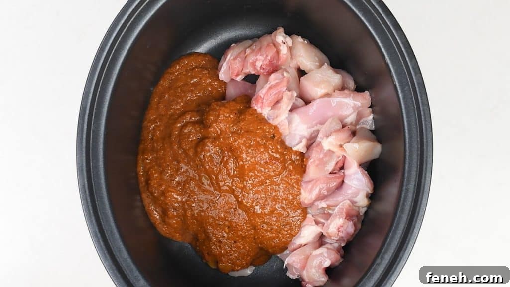 Raw, diced chicken pieces and a thick, brownish-orange sauce sit side by side in a black slow cooker, ready to become a flavorful Slow Cooker Chicken Curry—an easy curry recipe perfect for busy days.