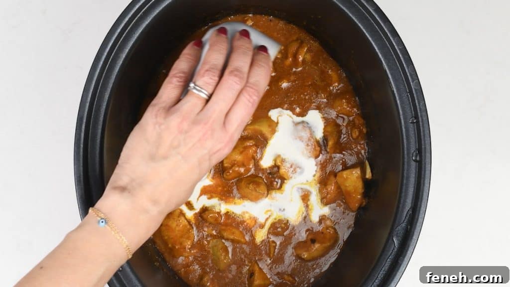 A hand with red nail polish pours cream into a slow cooker filled with a rich brown curry containing potatoes and mushrooms—an easy curry recipe perfect for making Slow Cooker Chicken Curry at home.
