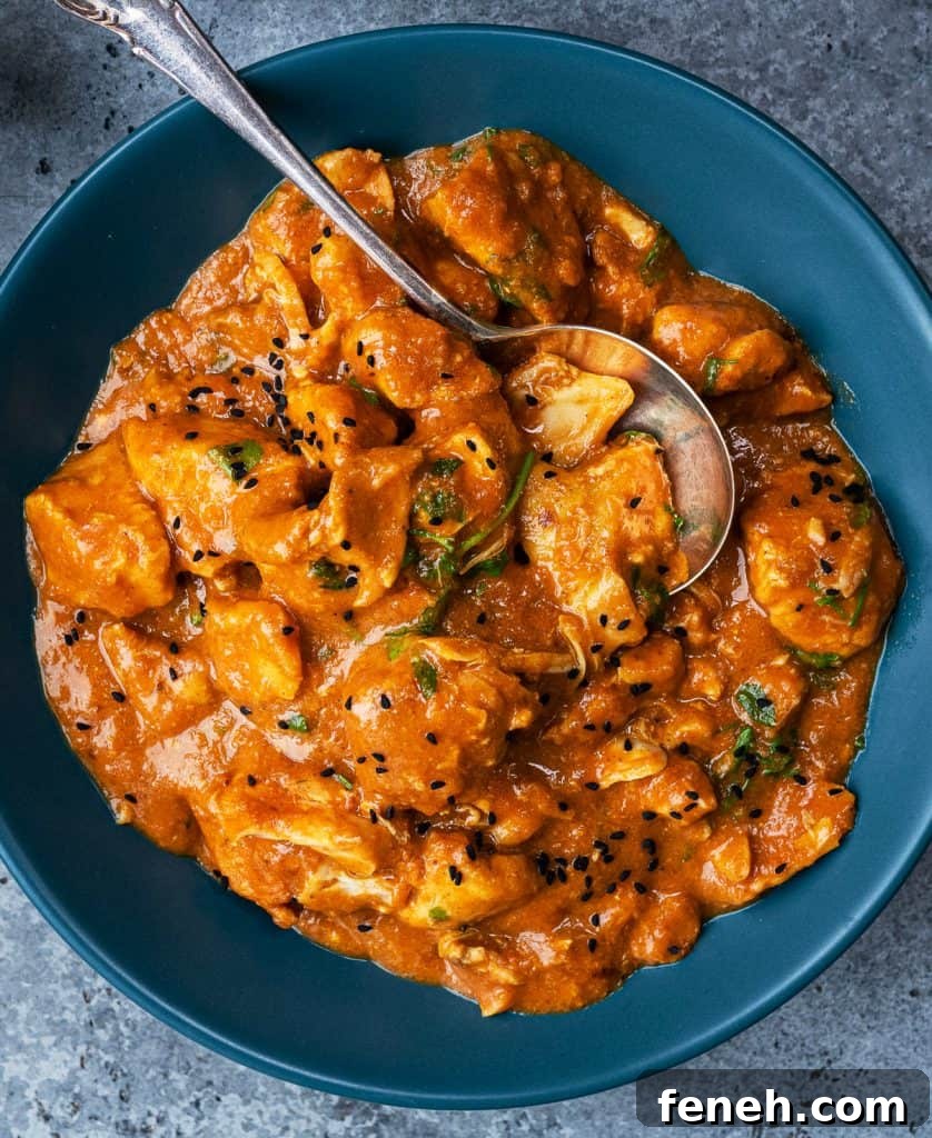 A blue bowl filled with creamy orange Slow Cooker Chicken Curry, garnished with black sesame seeds and herbs, with a silver spoon resting inside—a perfect easy curry recipe for any occasion.