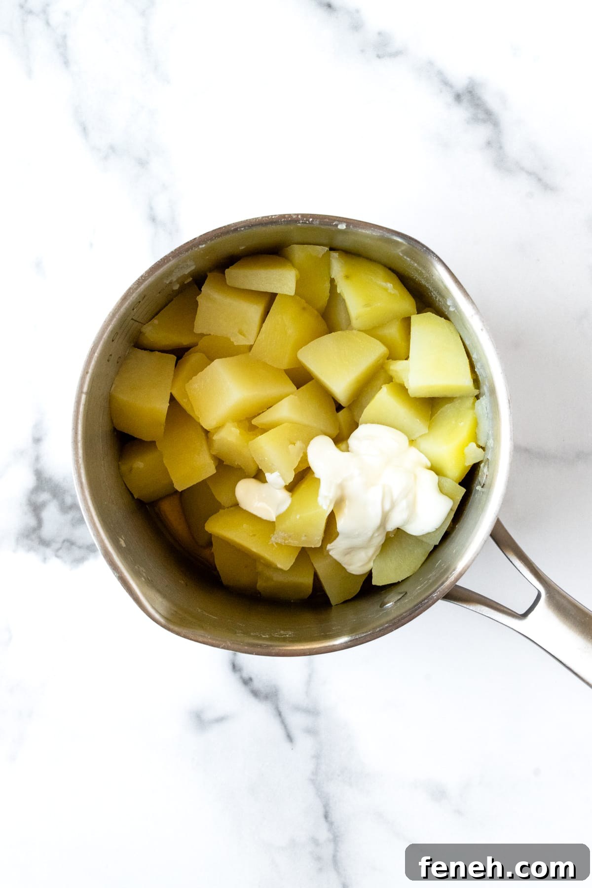 Cooked potato chunks in a pot with sour cream ready to be mashed.