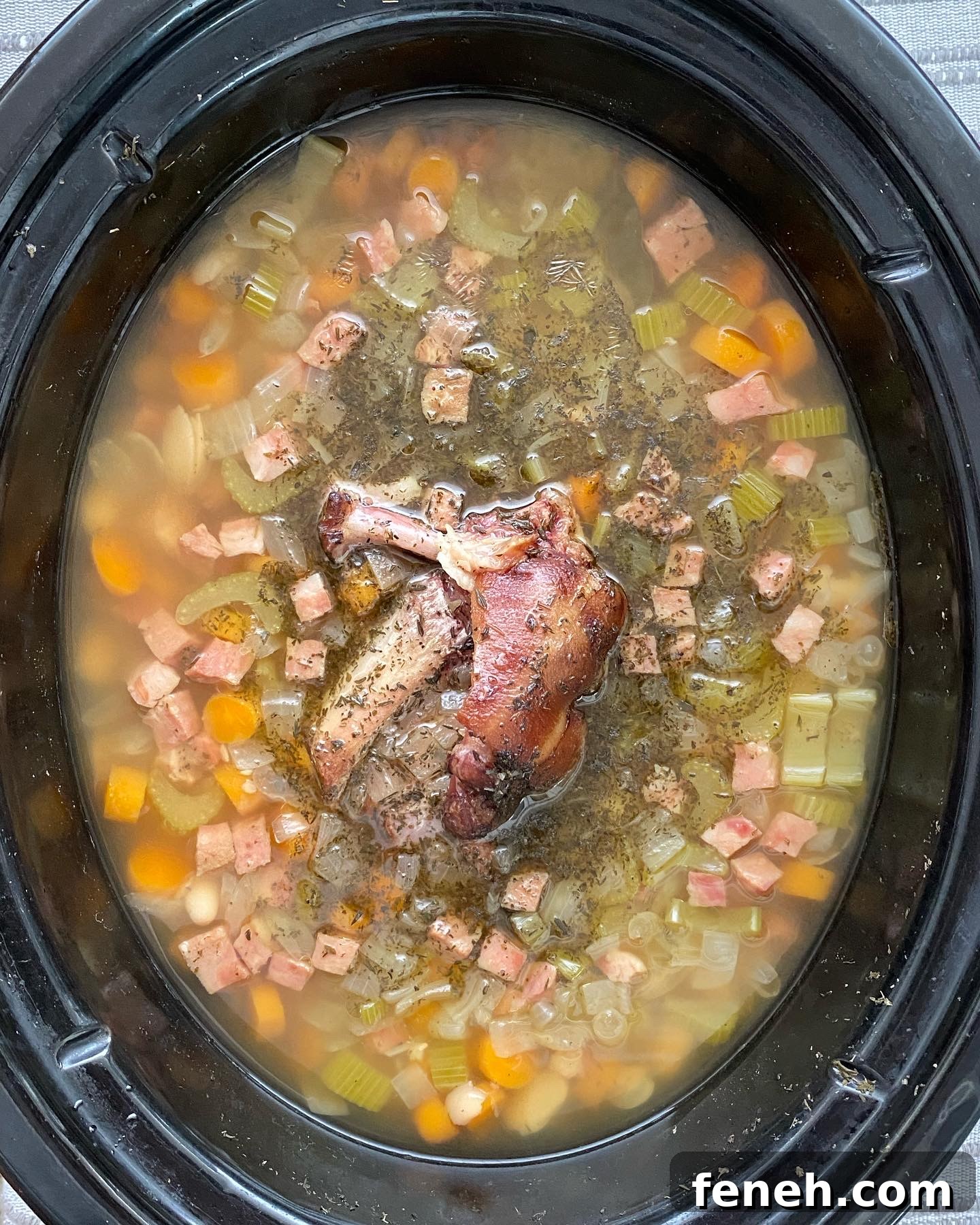 overhead shot of cooked crockpot ham and bean soup in a black slow cooker