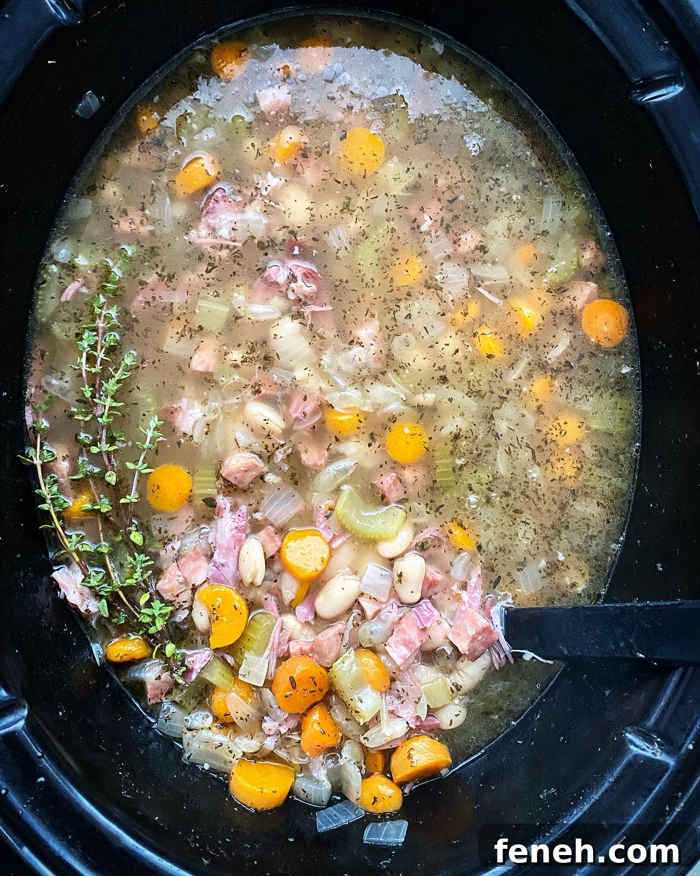 overhead shot of cooked crockpot ham and bean soup in a black slow cooker garnished with fresh thyme