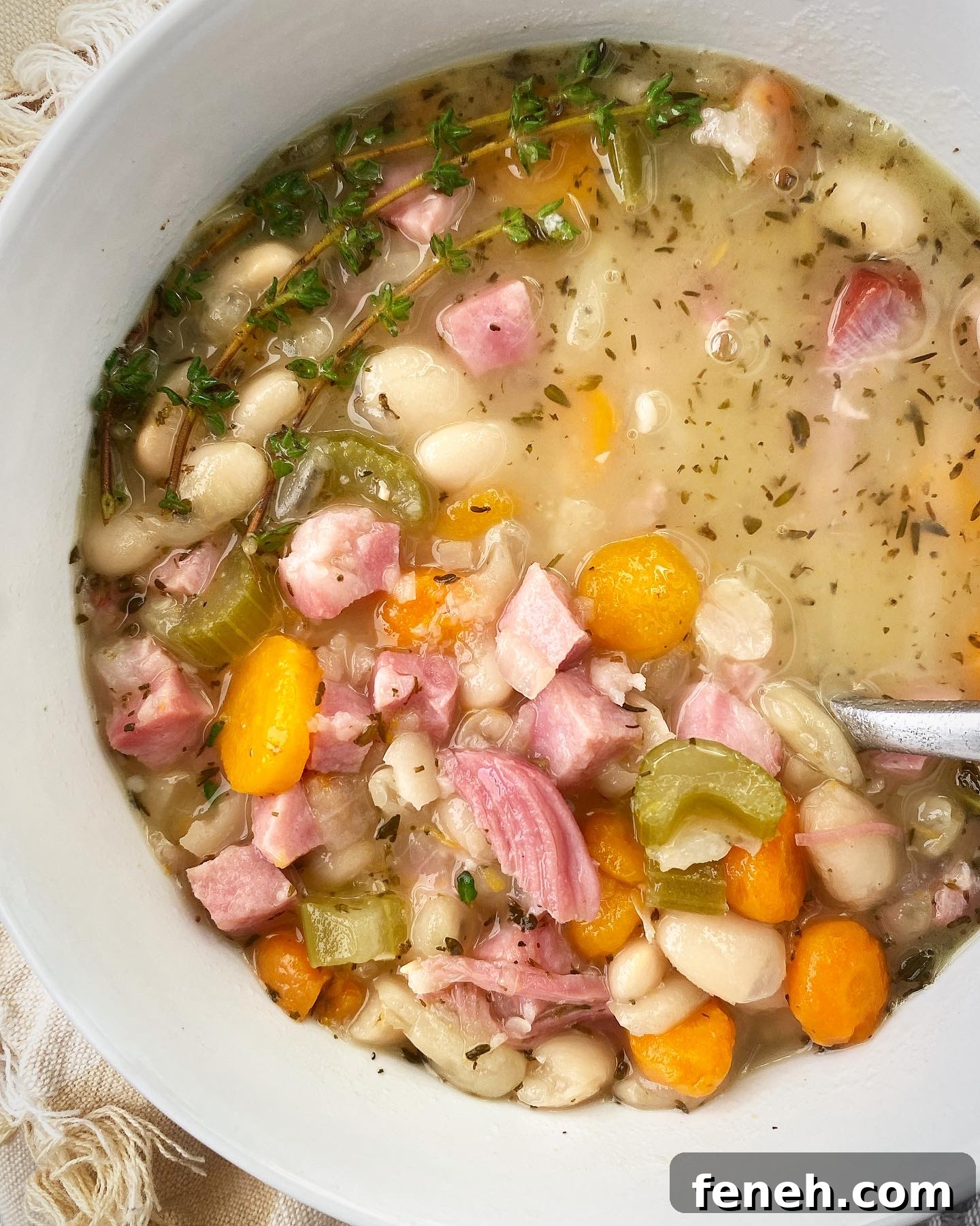 close up shot of slow cooker ham and bean soup in a white bowl garnished with fresh thyme