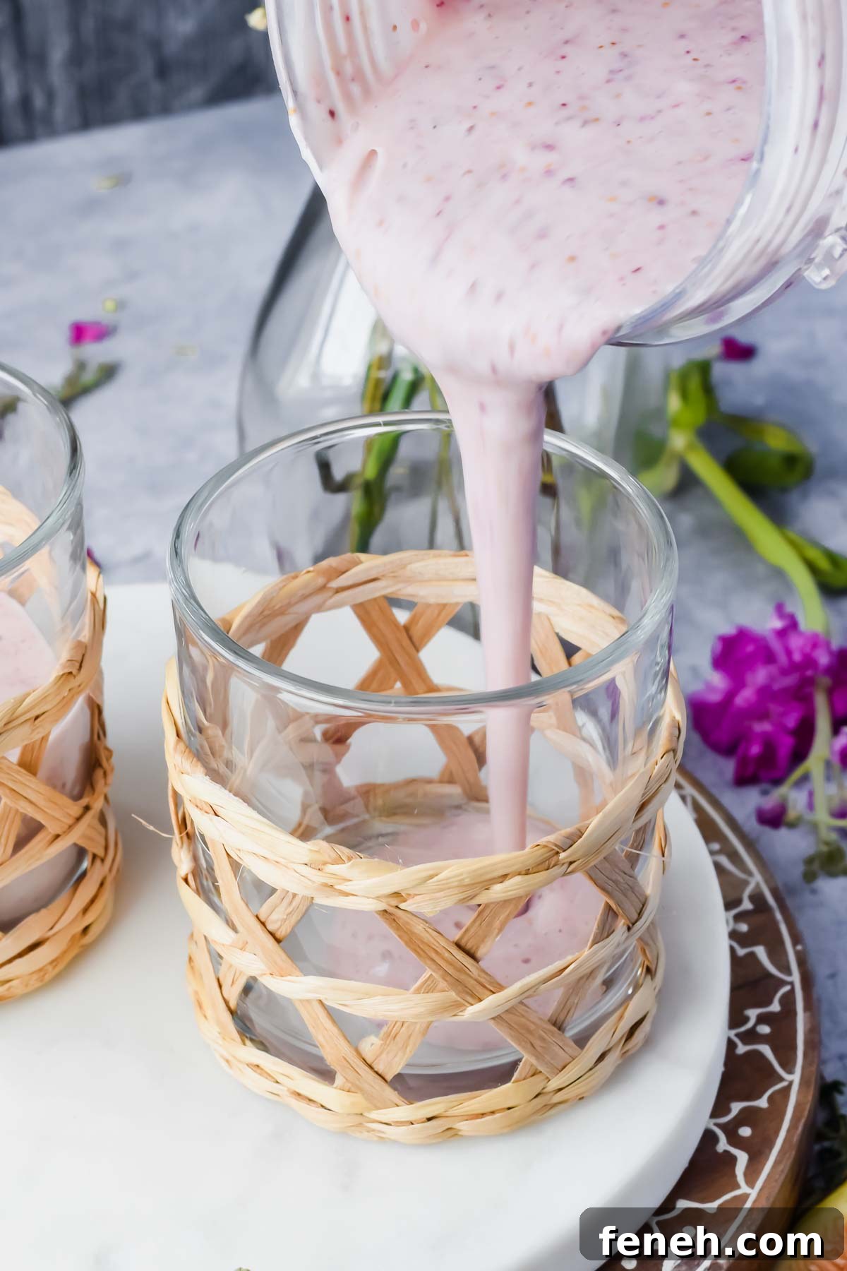 blender pouring fig smoothie into a glass cup on a marble slab.