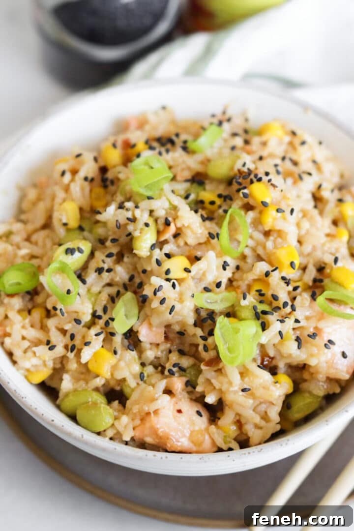 Salmon and rice bowl prepared in a white bowl and topped with black sesame seeds and green onions