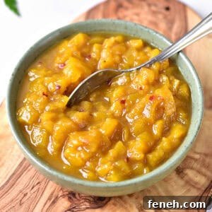 Greenish bowl with mango chutney and silver spoon. Wooden board surface.