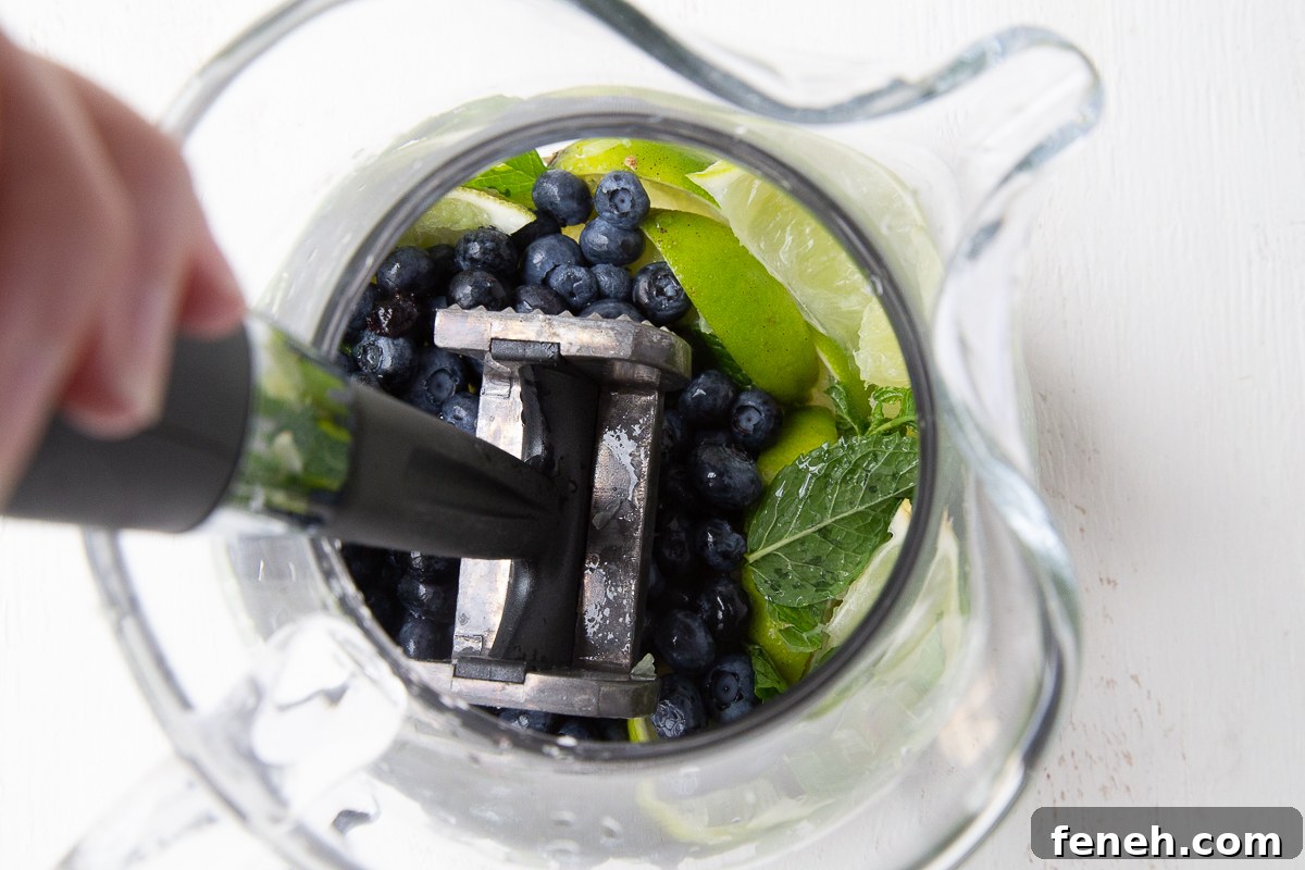 meat mallet smashing blueberries, lime, and mint in a glass pitcher