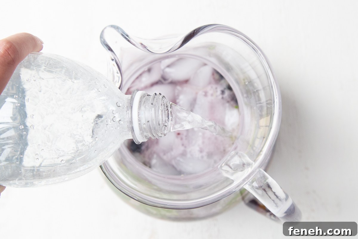 hand pouring club soda into a glass pitcher of mojitos
