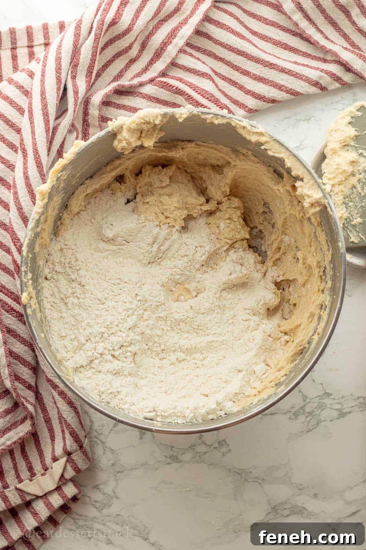 Flour in raw cookie dough batter in metal bowl.