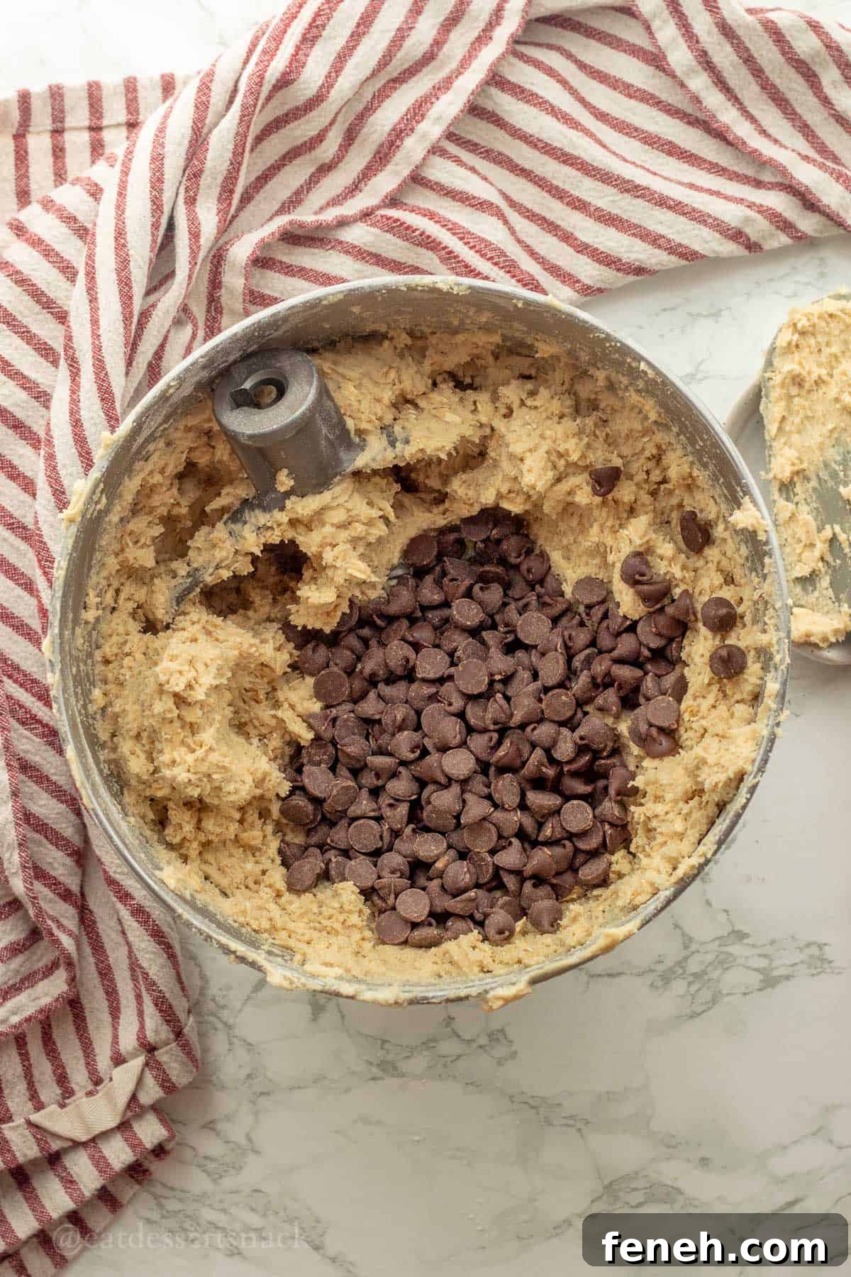 Chocolate chips in bowl of raw sourdough oatmeal cookie dough in metal mixing bowl.