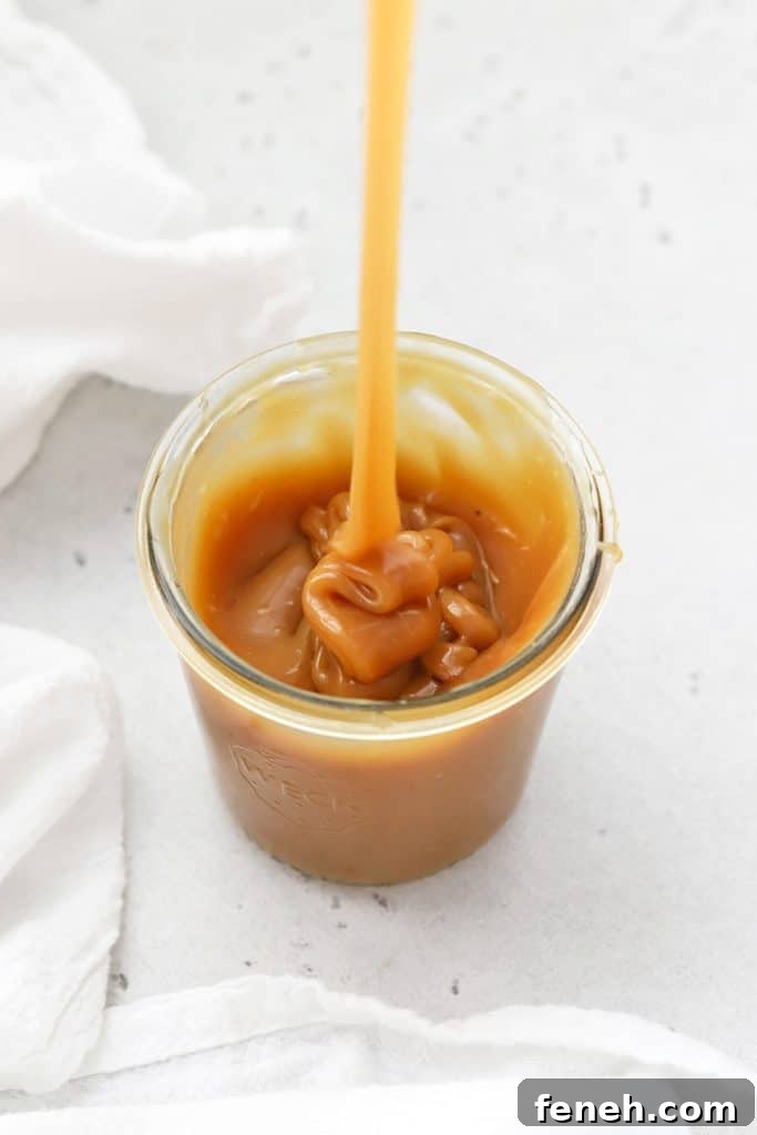 Pouring thick homemade caramel sauce into a jar