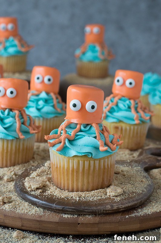 Seven easy vanilla Octopus Cupcakes covered in blue buttercream frosting on a round wooden board.